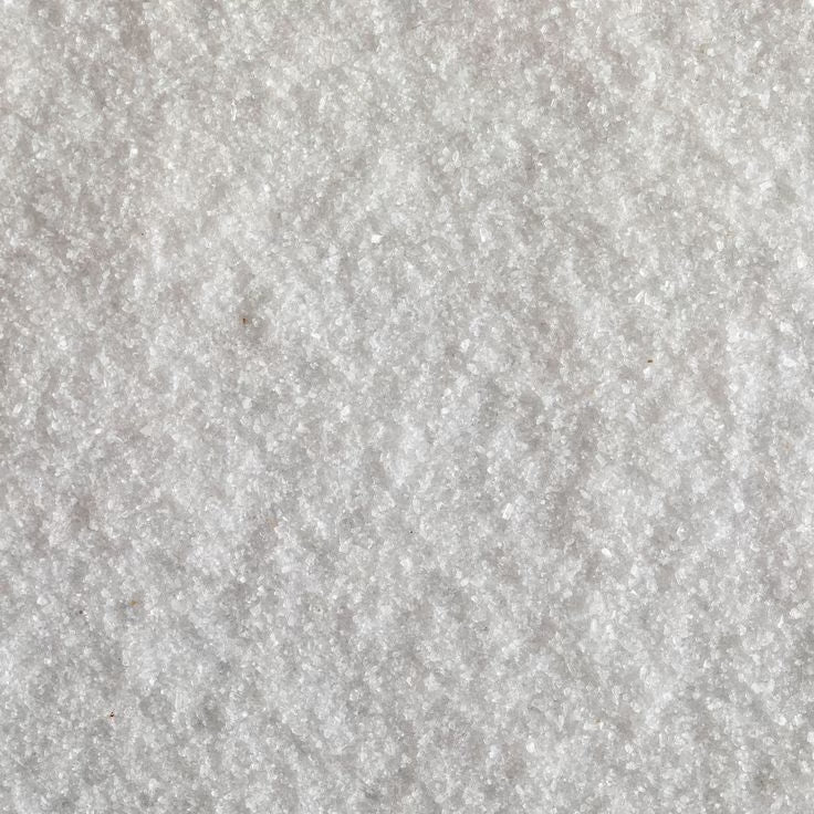 Close-up view of a white textured salt periodic element sodium (NA) surface with a crystalline appearance, resembling coarse salt or sugar crystals, creating a rough, grainy pattern.