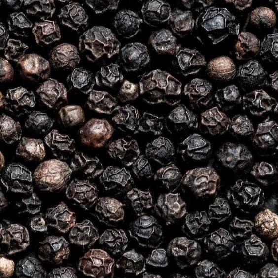 Close-up image of a pile of whole black peppercorns. The textured surface of the peppercorns is clearly visible, showcasing a variety of dark brown and black hues.
