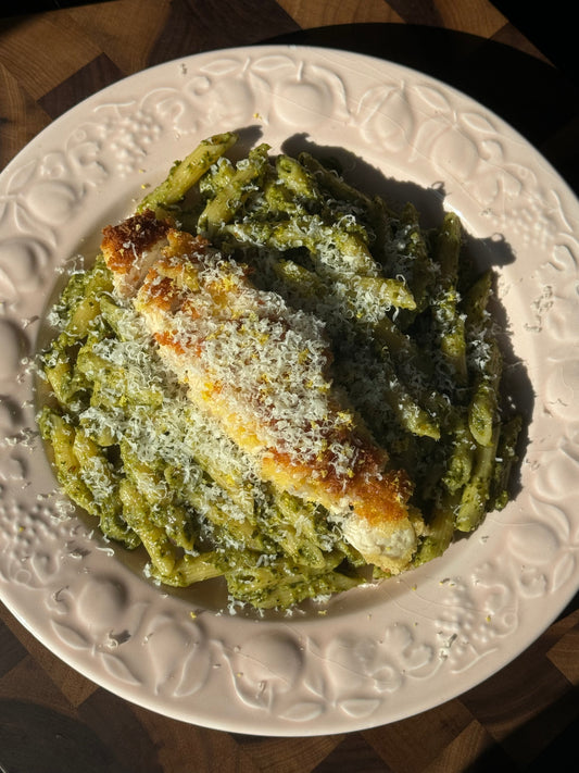 Crispy golden lemon chicken served over penne pasta tossed in vibrant green Besto sauce, garnished with fresh herbs.