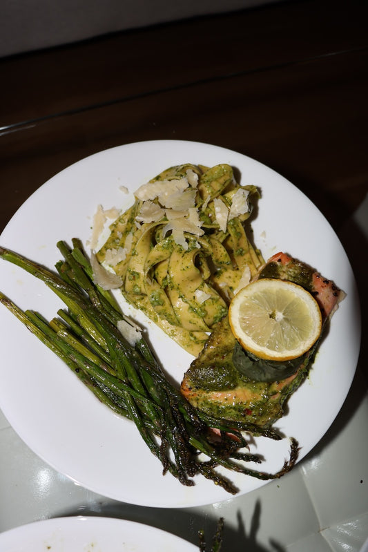 A healthy dinner meal of oven roasted asparagus, pesto pasta with parmesan cheese, and lemon salmon marinated in Besto pesto with a lemon slice on top.