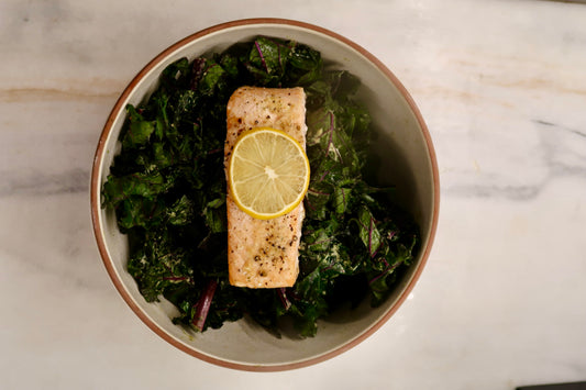 A bowl of a purple kale tahini salad dressing using Besto pesto and a filet of salmon with lemon for a healthy allergy friendly dinner.