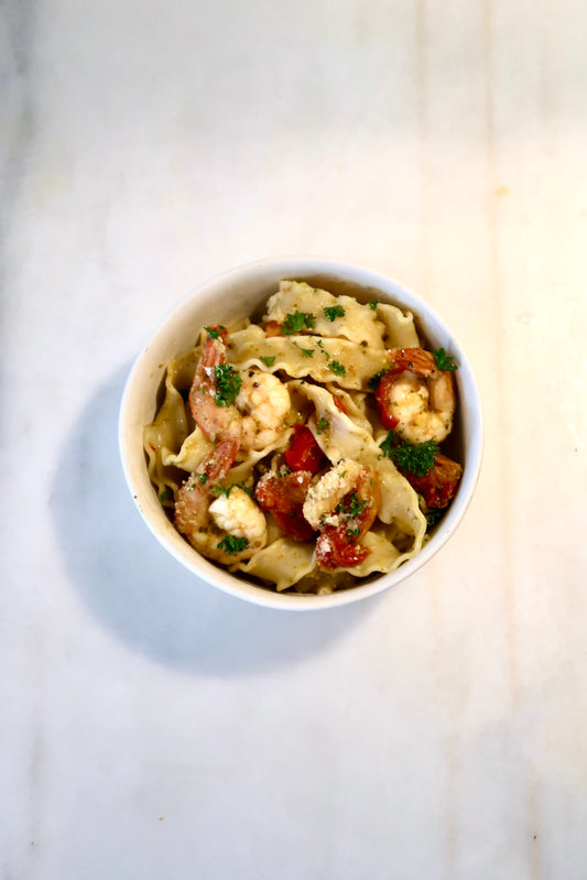 Shrimp, linguine pasta dish with curly parsley and Besto pesto mixed all together. Cherry tomatos and parmesan cheese are in the meal.